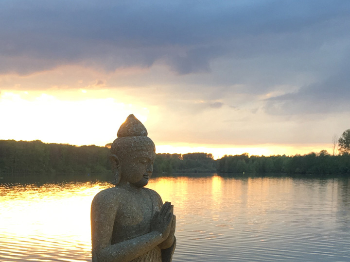 Blick in den Sonnenuntergang über den See mit Steinstatue im Vordergrund am Vabali Spa Düsseldorf